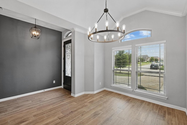 unfurnished dining area with an inviting chandelier, wood finished floors, crown molding, baseboards, and vaulted ceiling