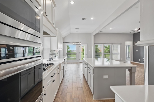 kitchen featuring light wood-style flooring, stainless steel appliances, a kitchen island, light countertops, and gray cabinets
