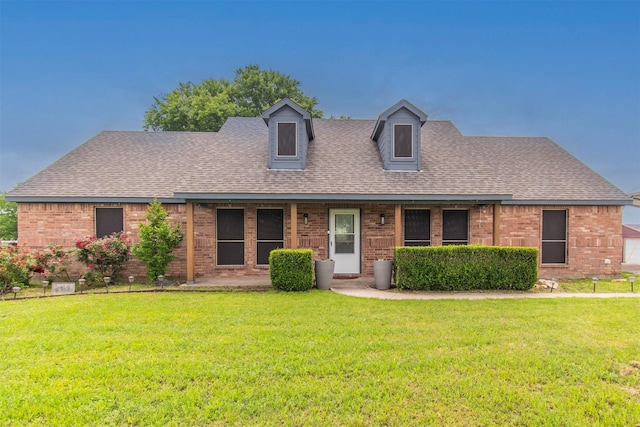new england style home featuring brick siding, roof with shingles, and a front lawn
