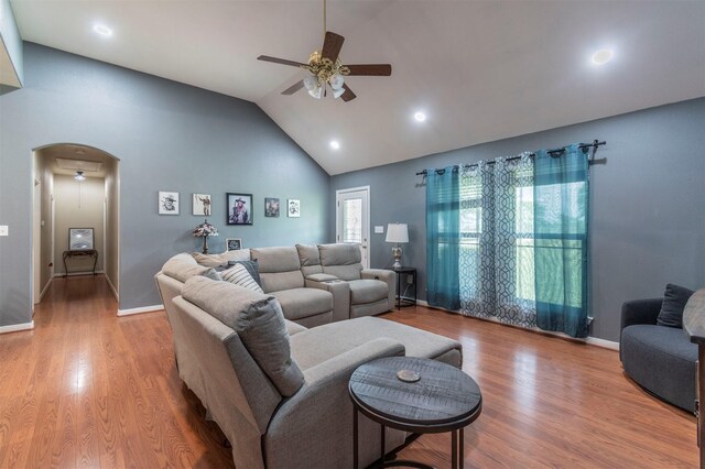 living room with ceiling fan, arched walkways, high vaulted ceiling, baseboards, and wood finished floors