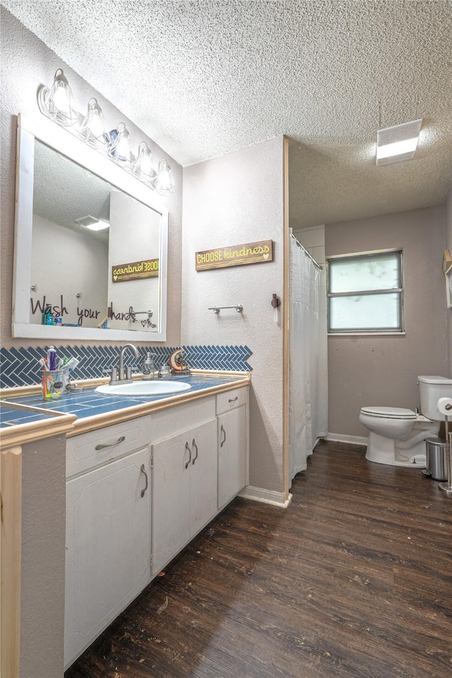 full bath with vanity, a textured ceiling, wood finished floors, and toilet