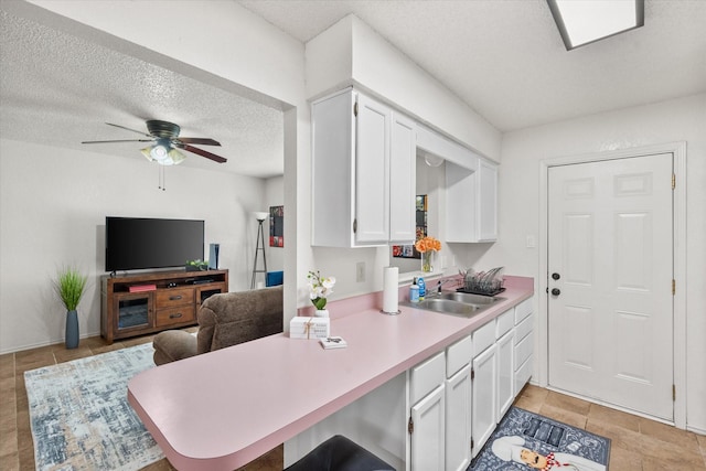 kitchen with white cabinets, a sink, light countertops, a ceiling fan, and a peninsula