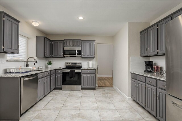 kitchen with recessed lighting, light stone counters, a sink, appliances with stainless steel finishes, and gray cabinetry