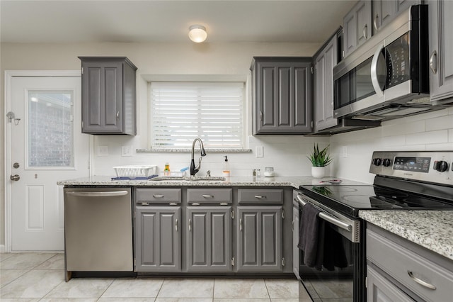kitchen with tasteful backsplash, gray cabinetry, light tile patterned floors, a sink, and stainless steel appliances