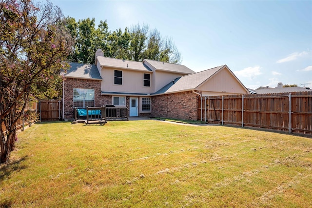 back of house with a yard, brick siding, a chimney, and a fenced backyard