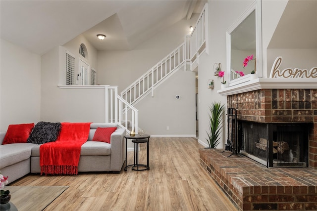 living area with baseboards, a brick fireplace, stairs, and wood finished floors