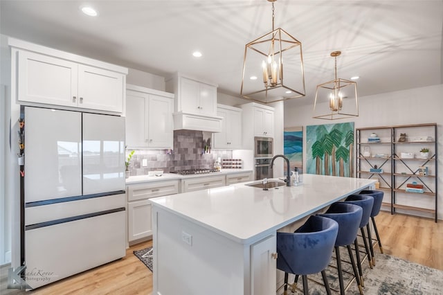 kitchen featuring a sink, light wood finished floors, a chandelier, stainless steel appliances, and white cabinetry