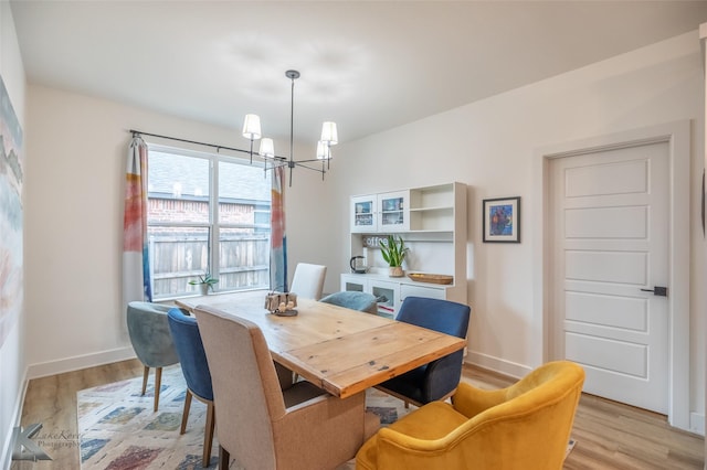 dining space with baseboards, a chandelier, and light wood-style floors