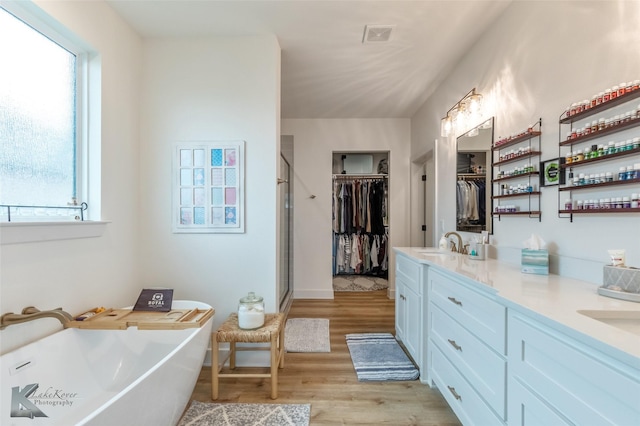 bathroom with double vanity, a freestanding tub, a sink, and wood finished floors
