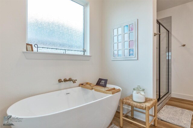 bathroom featuring a soaking tub, baseboards, a shower stall, and wood finished floors
