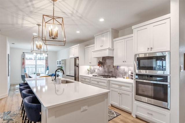 kitchen featuring tasteful backsplash, a center island with sink, a sink, a notable chandelier, and stainless steel appliances