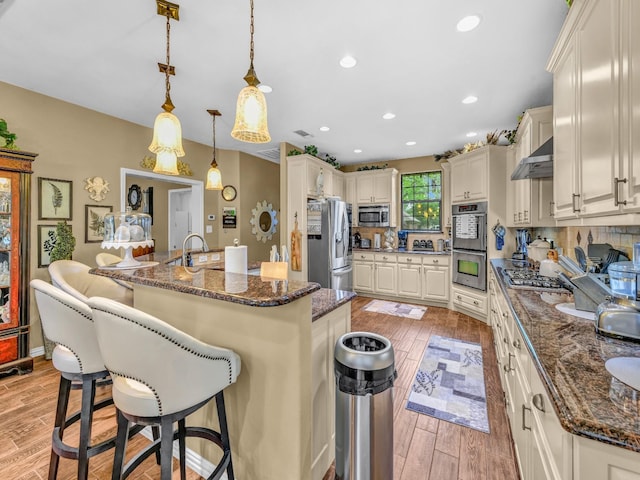 kitchen with a breakfast bar area, extractor fan, appliances with stainless steel finishes, and light wood-style floors