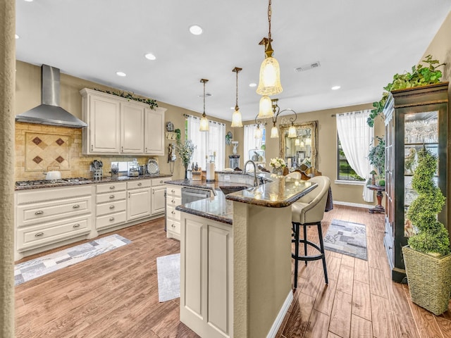 kitchen with visible vents, light wood-style floors, wall chimney exhaust hood, a sink, and stainless steel appliances