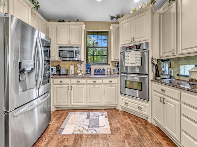 kitchen with appliances with stainless steel finishes, decorative backsplash, light wood-style flooring, and dark stone countertops