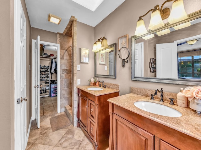 bathroom with a sink, a walk in closet, a tile shower, and two vanities