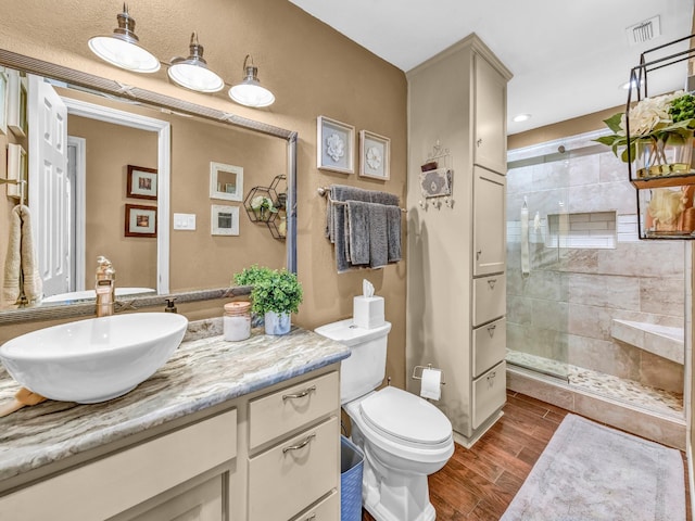 full bathroom with vanity, toilet, wood finished floors, visible vents, and tiled shower