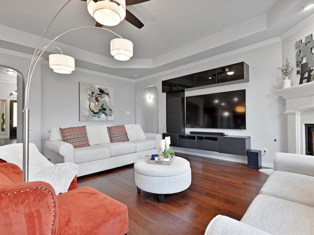 living area with ornamental molding, hardwood / wood-style floors, ceiling fan, a raised ceiling, and arched walkways