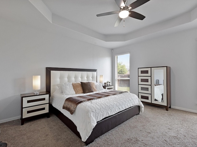 carpeted bedroom with a ceiling fan, a tray ceiling, and baseboards
