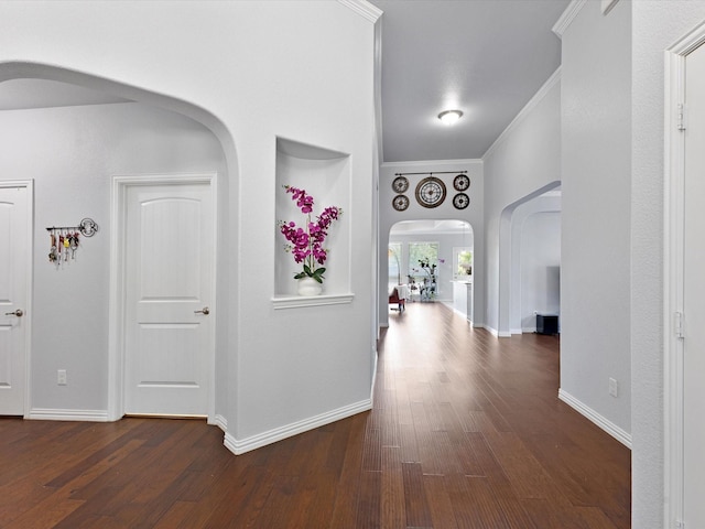 hall with arched walkways, baseboards, ornamental molding, and dark wood-type flooring