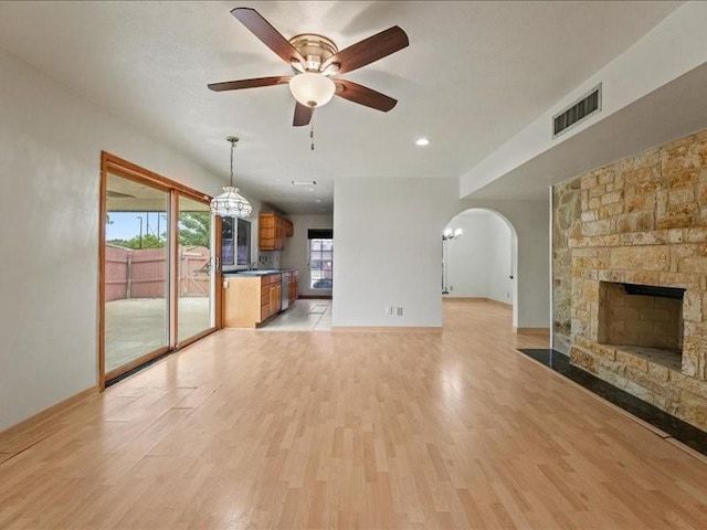unfurnished living room featuring arched walkways, a stone fireplace, a ceiling fan, light wood-type flooring, and visible vents