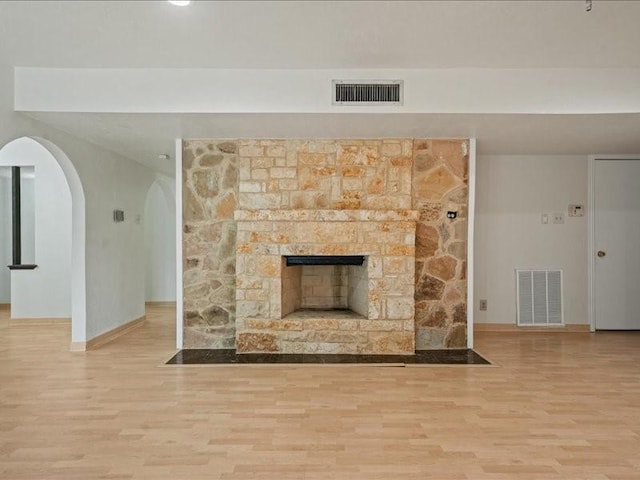 unfurnished living room with visible vents, arched walkways, baseboards, and wood finished floors