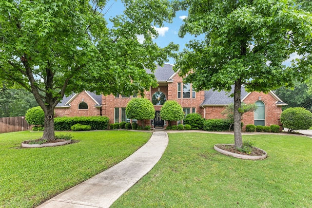 view of front of home with fence, a shingled roof, a front lawn, and brick siding