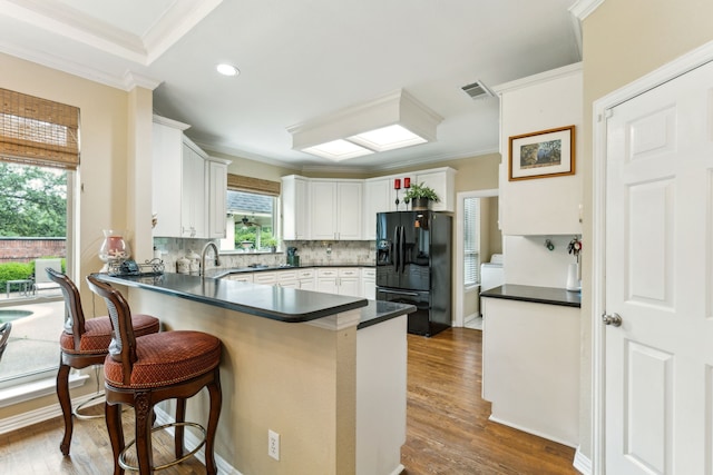 kitchen with crown molding, dark countertops, a peninsula, visible vents, and black fridge with ice dispenser