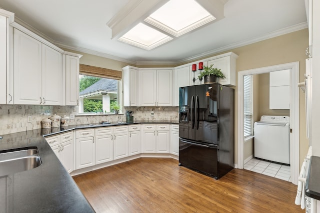 kitchen with washer / clothes dryer, dark countertops, black fridge with ice dispenser, light wood-type flooring, and white cabinets
