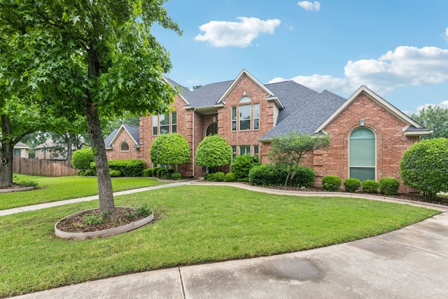 view of front facade featuring brick siding, fence, a shingled roof, and a front yard