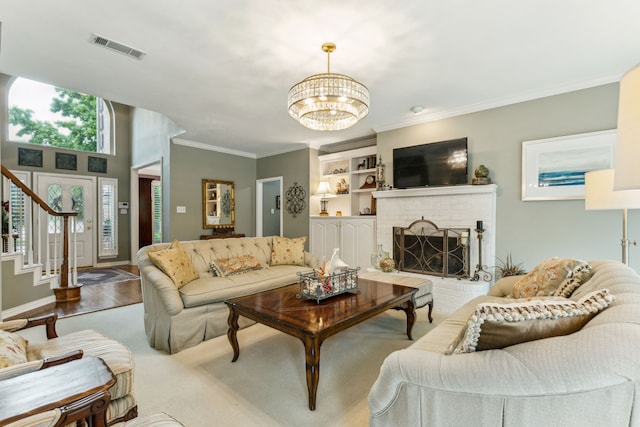living area featuring an inviting chandelier, crown molding, a brick fireplace, and stairway