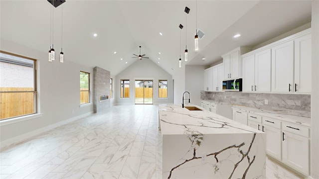 kitchen with a sink, marble finish floor, a ceiling fan, stainless steel microwave, and a center island with sink