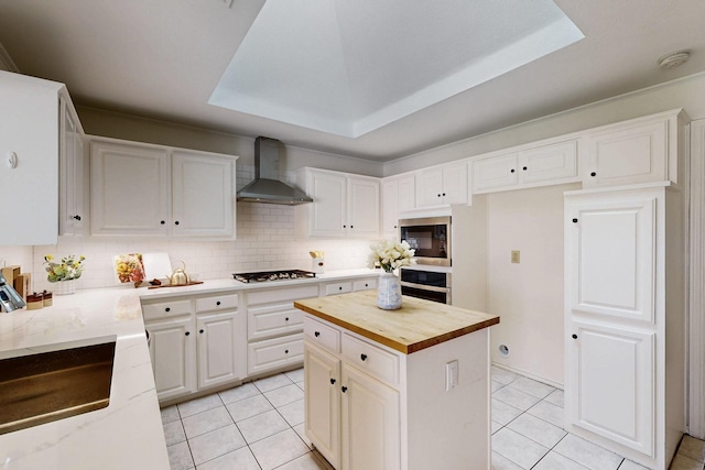 kitchen with wall chimney range hood, butcher block countertops, light tile patterned flooring, and tasteful backsplash