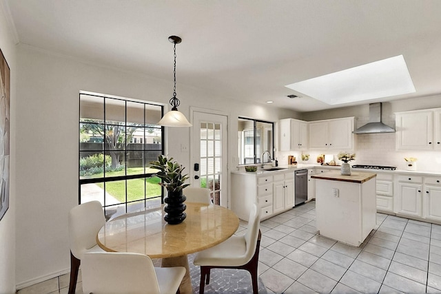 kitchen with wall chimney range hood, a sink, stainless steel dishwasher, a kitchen island, and gas cooktop