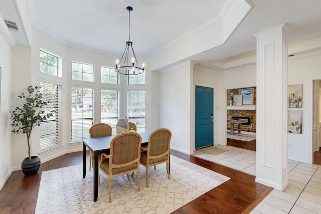 dining area with hardwood / wood-style floors, a chandelier, ornate columns, ornamental molding, and a fireplace