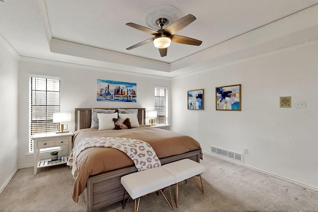 carpeted bedroom with a tray ceiling, ornamental molding, multiple windows, and baseboards