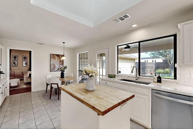 kitchen with stainless steel dishwasher, wooden counters, a sink, white cabinetry, and a kitchen island