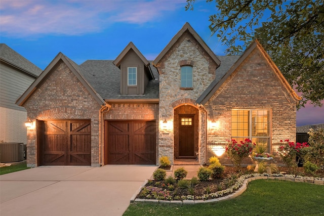 french provincial home with concrete driveway, brick siding, central AC, and roof with shingles