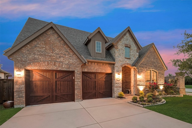 french country style house featuring stone siding, roof with shingles, brick siding, concrete driveway, and a lawn