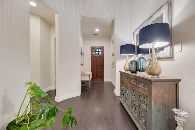 hall featuring dark wood-type flooring, ornamental molding, baseboards, and visible vents