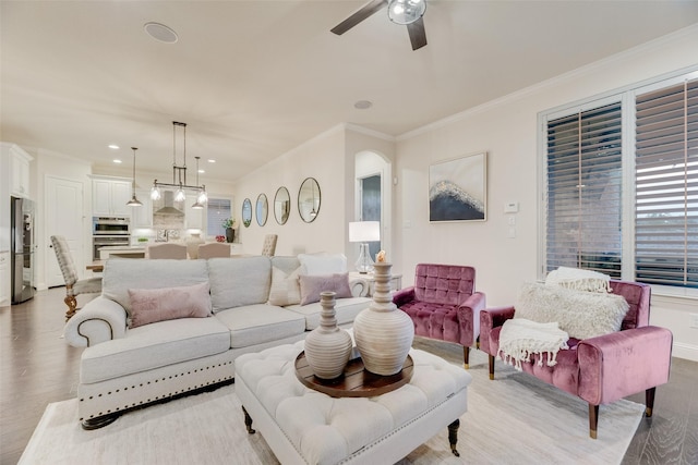 living room with ornamental molding, ceiling fan, light wood-type flooring, recessed lighting, and arched walkways