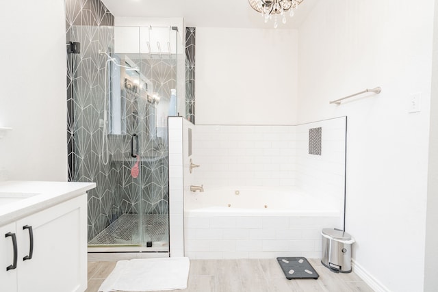 bathroom featuring an inviting chandelier, vanity, a tub with jets, wood finished floors, and a stall shower