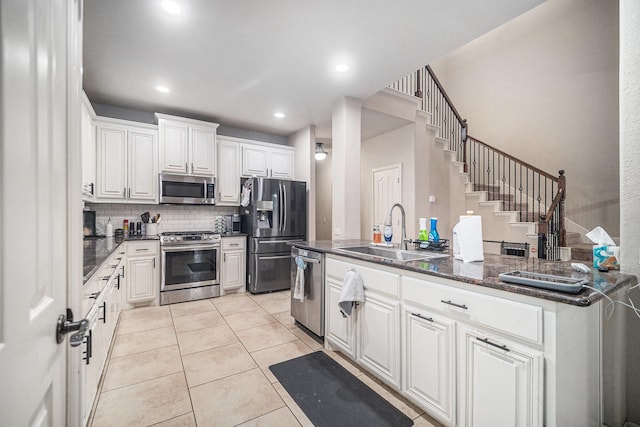 kitchen featuring stainless steel appliances, a sink, backsplash, white cabinetry, and light tile patterned floors