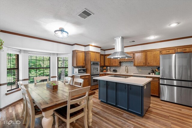 kitchen featuring light countertops, brown cabinetry, stainless steel appliances, island range hood, and visible vents