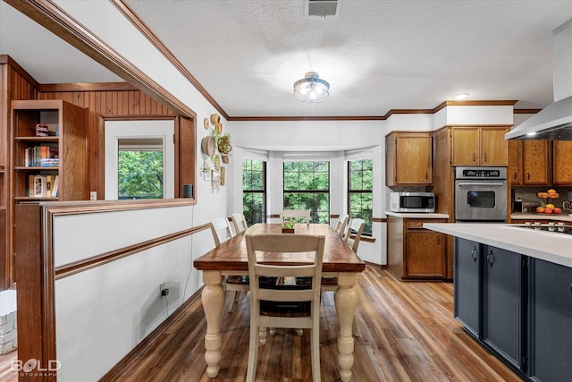 kitchen with brown cabinetry, visible vents, light wood-type flooring, wall chimney exhaust hood, and appliances with stainless steel finishes