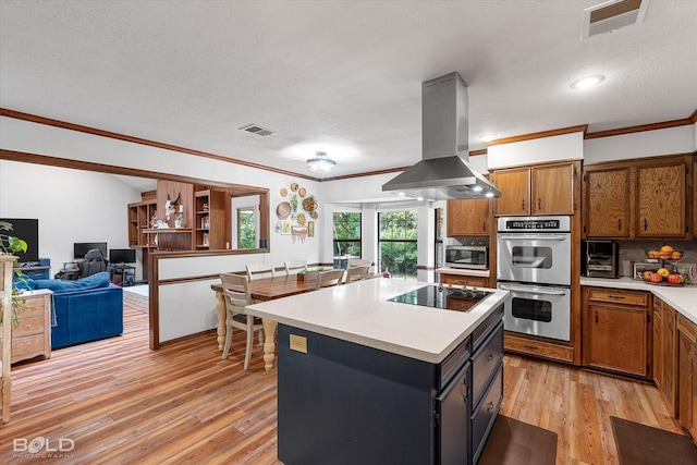 kitchen featuring island exhaust hood, appliances with stainless steel finishes, brown cabinets, light countertops, and light wood finished floors