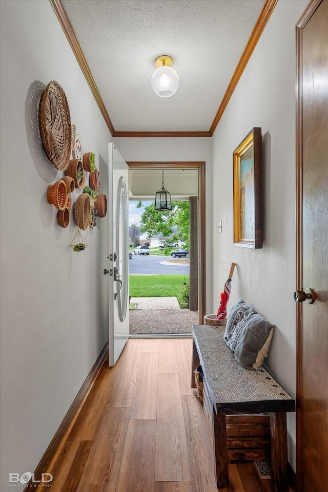 doorway featuring baseboards, a textured ceiling, ornamental molding, and wood finished floors