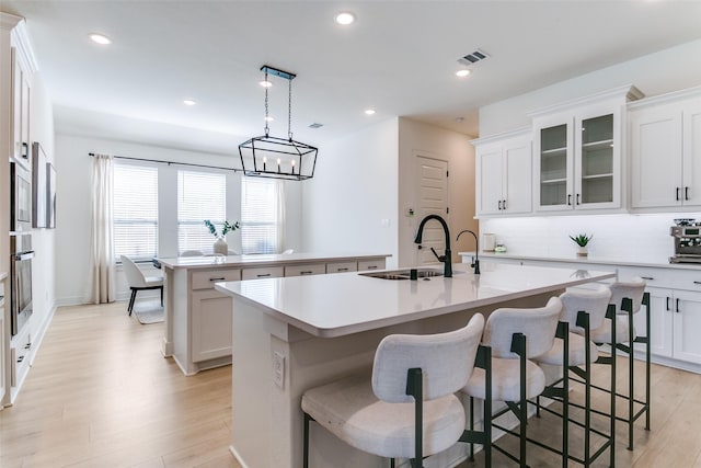 kitchen featuring visible vents, a center island with sink, a sink, light wood-style floors, and oven
