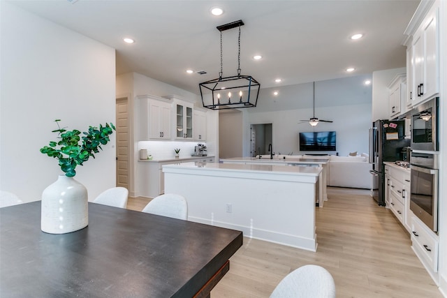 kitchen with white cabinets, ceiling fan with notable chandelier, stainless steel appliances, open floor plan, and a center island with sink