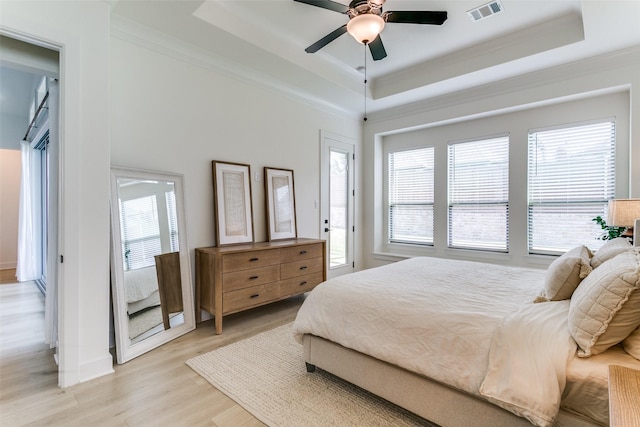 bedroom with visible vents, a raised ceiling, crown molding, and light wood-style floors