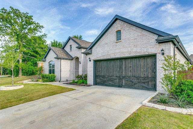 french country inspired facade with brick siding, an attached garage, a front yard, and concrete driveway